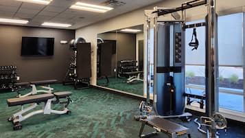 Un gimnasio con equipos de ejercicio variados, una banca y un espejo grande.