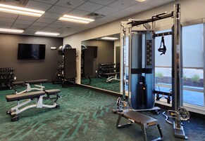 Un gimnasio con equipos de ejercicio variados, una banca y un espejo grande.