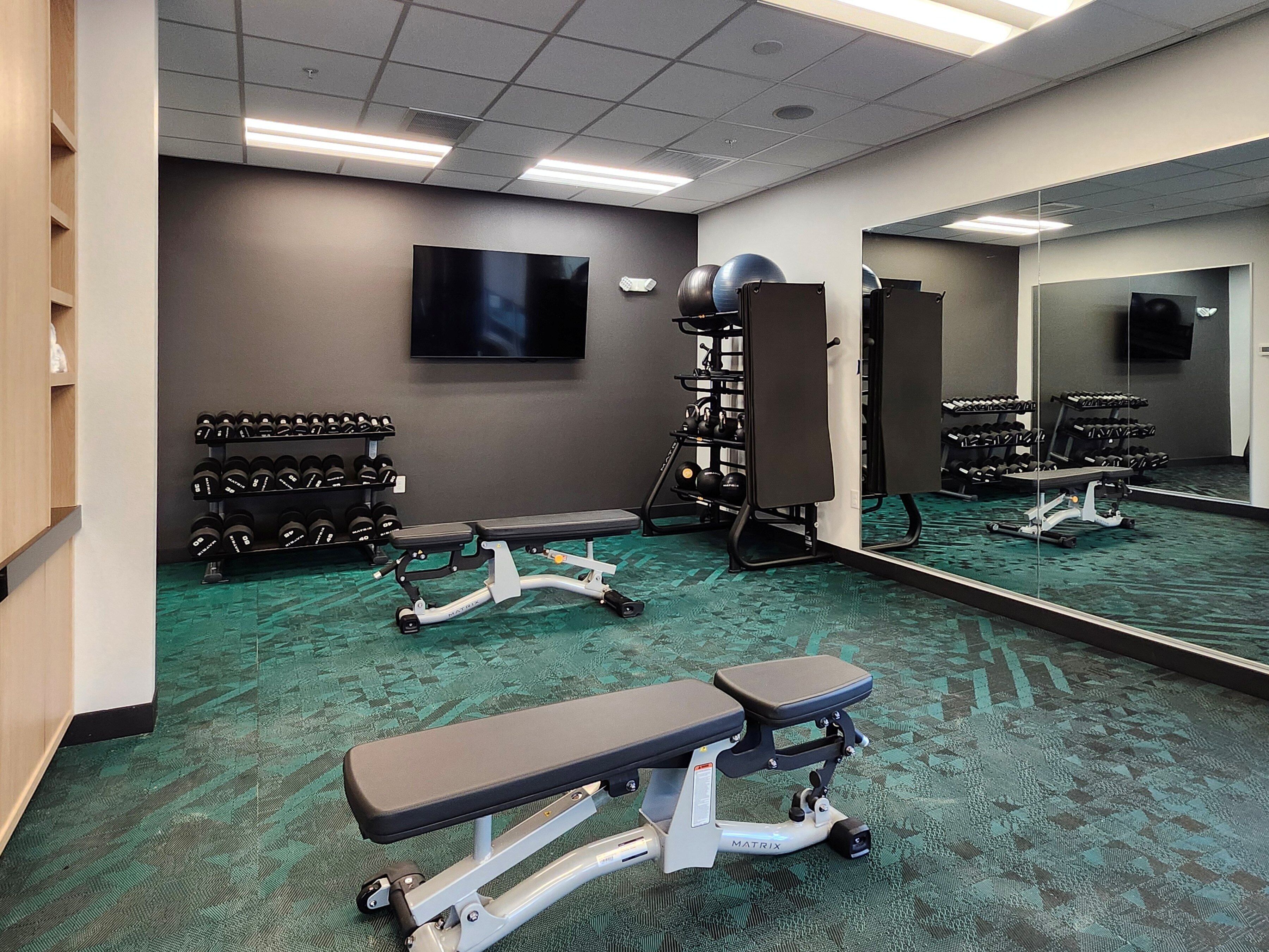 Un gimnasio con equipo de ejercicio, un televisor y un espejo grande.