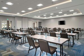 A conference room with multiple tables and chairs, equipped with water bottles, and a flat-screen TV mounted on the wall.