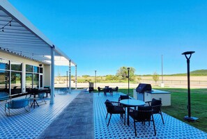 Ein Außenbereich mit Terrassentischen und -stühlen, einer überdachten Sitzgelegenheit und Blick auf die Landschaft.