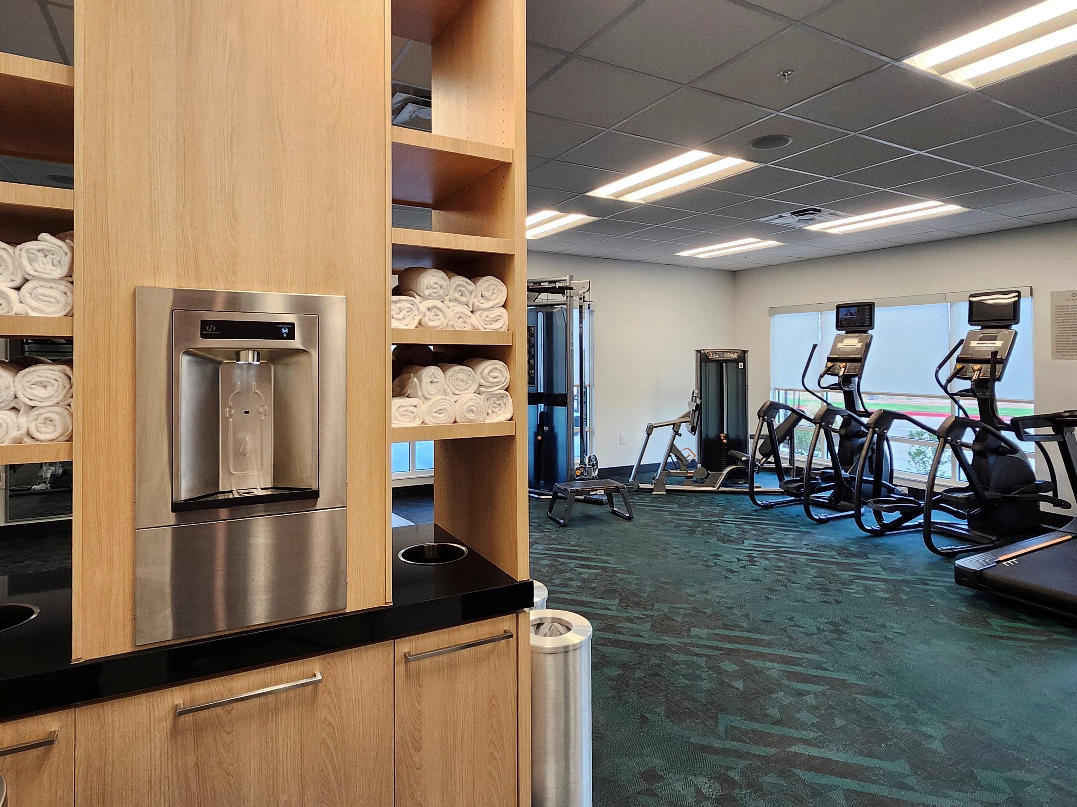 A gym with exercise equipment, a water dispenser, and towels on shelves.