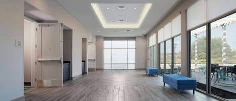 A spacious hallway with a modern design, featuring a wooden floor, large windows, and a seating area with blue sofas.