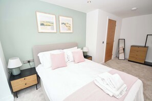 Un dormitorio ordenado con cama, mesitas de noche, lámpara, espejo y armario.