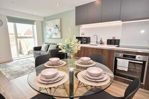 Una cocina moderna con horno integrado y una zona de comedor con mesa de vidrio preparada para cuatro.