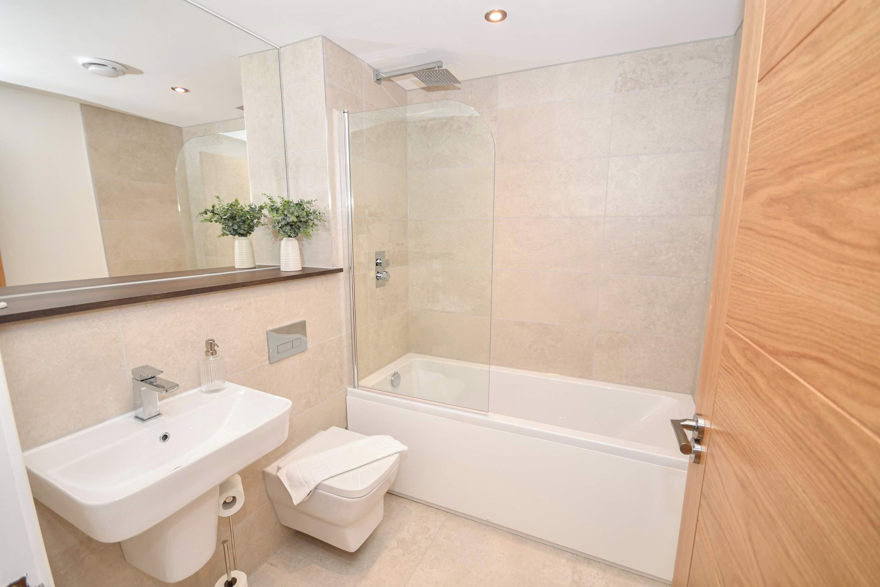 A modern bathroom with a glass-enclosed shower, a white sink, and a wooden door.