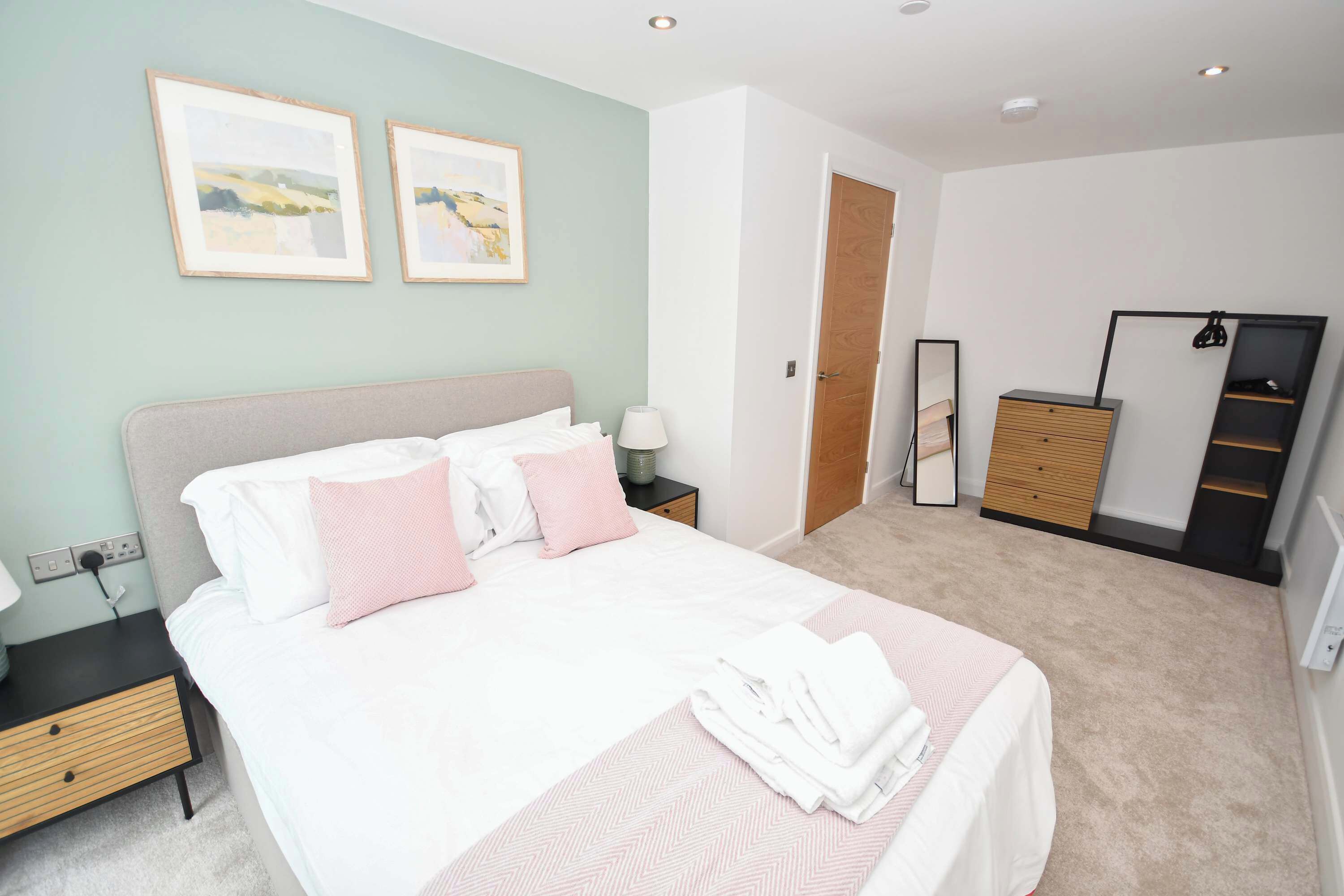 A neatly arranged bedroom with a bed, bedside tables, a wardrobe, and a mirror.