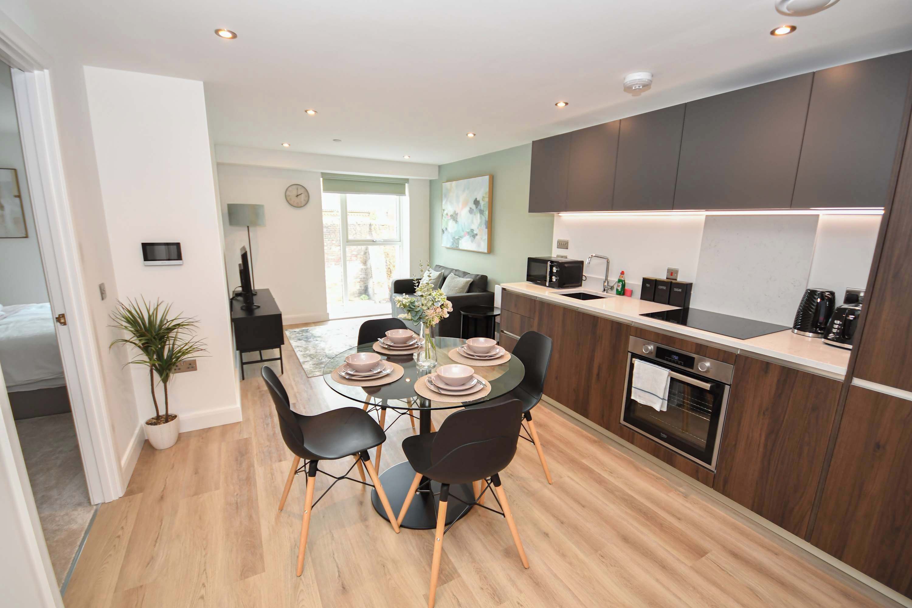 A modern kitchen with a dining area, wooden flooring, and a large window.