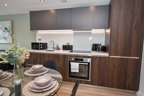 A modern kitchen with dark wood cabinets, a built-in microwave, a coffee maker, and a stove. - Bright & Contemporary 1 Bedroom Apartment in Leeds (Leeds)