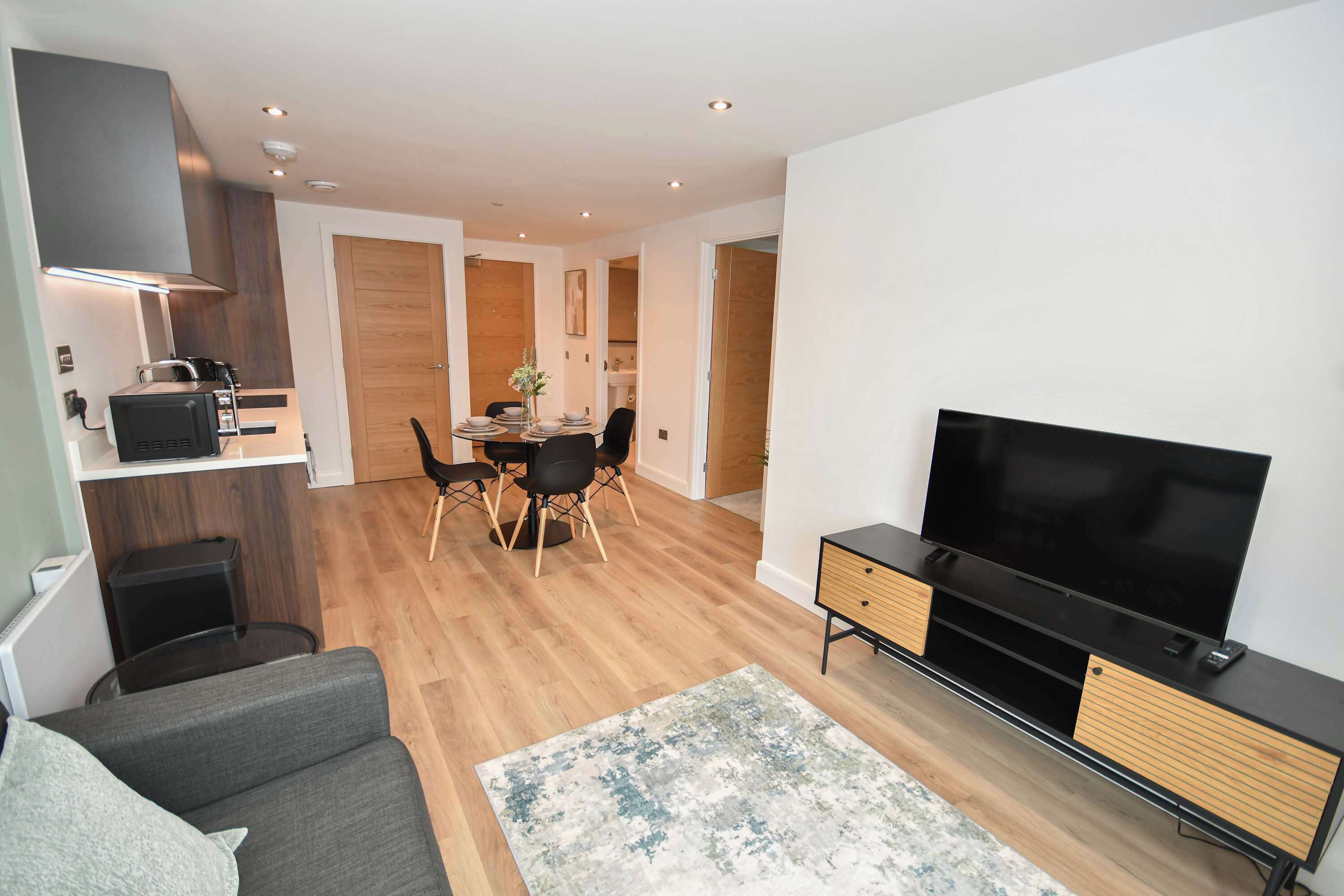 A modern living room with a flat-screen TV, a sofa, and a dining area with a table and chairs.