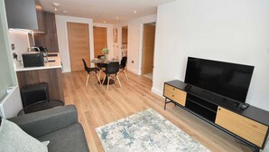 Uma sala de estar moderna com televisão de tela plana, um sofá e uma área de jantar com mesa e cadeiras.