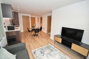 A modern living room with a flat-screen TV, a sofa, and a dining area with a table and chairs. - Bright & Contemporary 1 Bedroom Apartment in Leeds (Leeds)