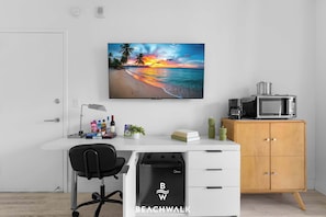 A modern office space with a desk, chair, and a large wall-mounted TV displaying a beach scene. - Beachwalk 2BR Resort Style - Intracoastal View (Hallandale Beach)