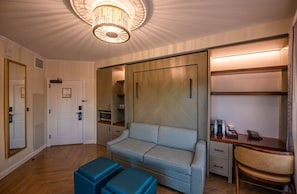 Une chambre d’hôtel équipée d’un canapé, d’un bureau, d’une chaise, d’une armoire et d’un luminaire au plafond.