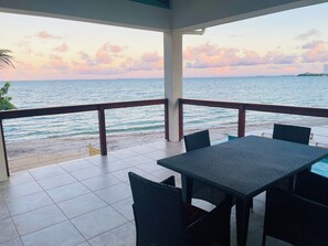 A terrace with a table and chairs overlooking a beach and ocean. - *Beachfront Placencia Village* off the Sidewalk! (Placencia)