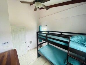 Une chambre avec un lit superposé, un ventilateur de plafond, des murs blancs, une porte et une fenêtre avec des rideaux.