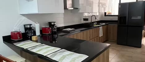 A modern kitchen with a central island, bar stools, and a refrigerator.