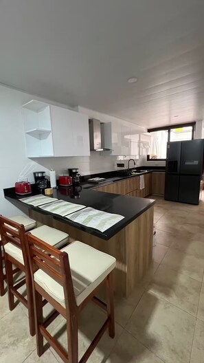 A modern kitchen with a central island, bar stools, and a refrigerator. - 103 Trabajo o Descanso Cómodo Hospedaje San José (San Jose)