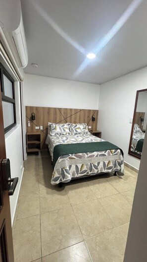 Une chambre à coucher avec un lit, des tables de chevet, un miroir et une porte.