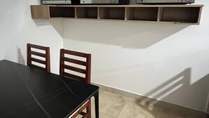 Una habitación con una mesa de comedor, dos sillas y un estante con tres microondas.