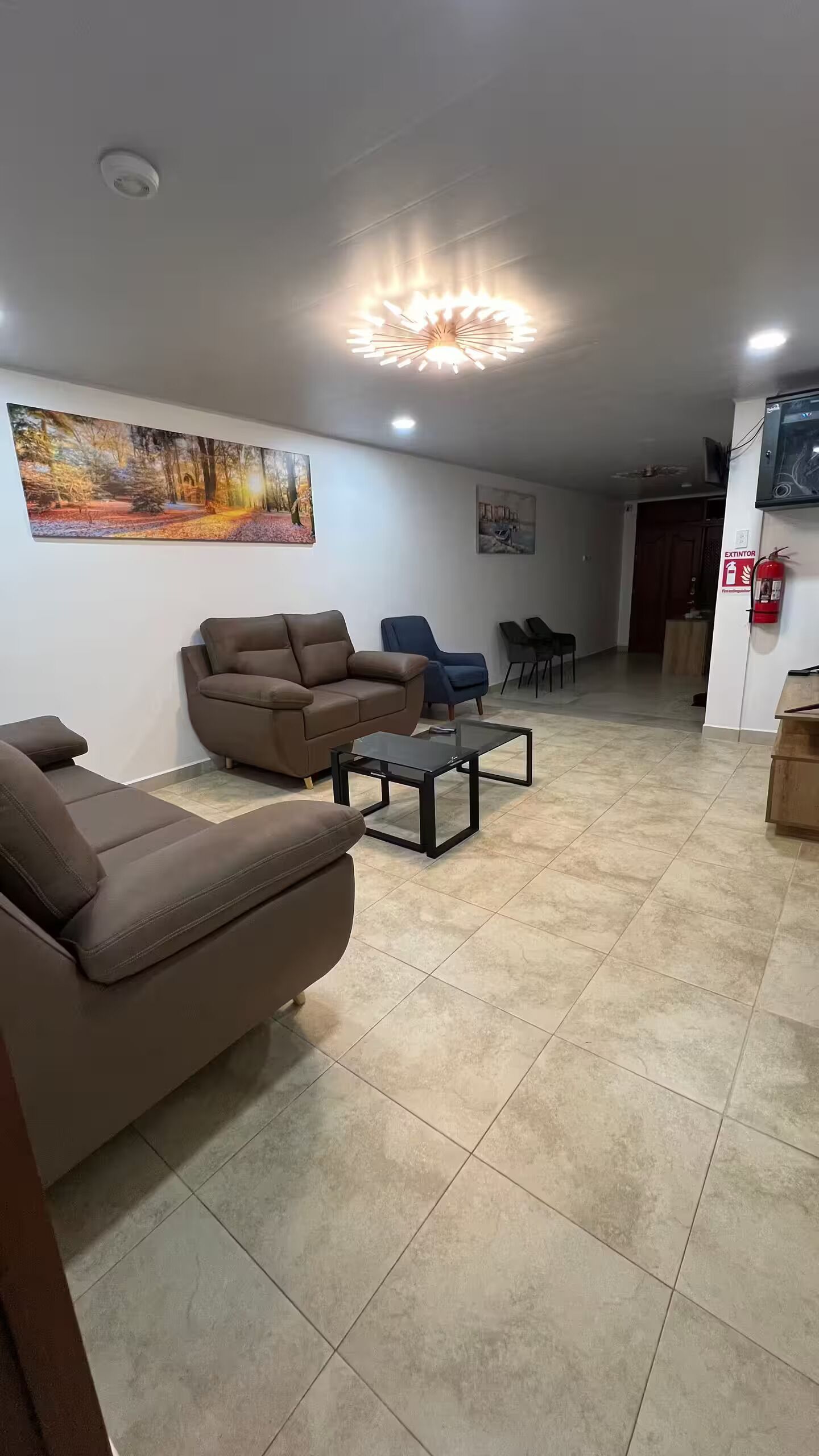 Un salon avec un canapé marron, une table basse en verre et un tableau accroché au mur.