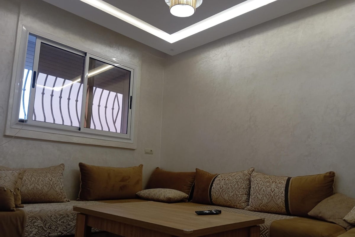 Habitación de esquina con sofá, mesa y ventana con barrotes.