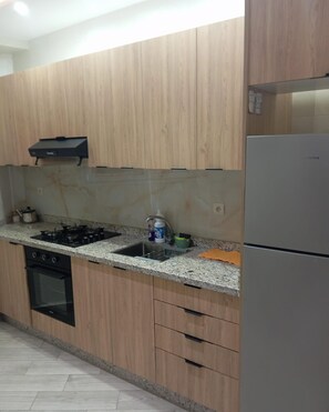 A kitchen with wooden cabinets, a gas stove, a sink, and a refrigerator.