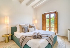 Une chambre à coucher avec un lit, des oreillers, une table de chevet, une lampe et une fenêtre donnant sur un paysage verdoyant.