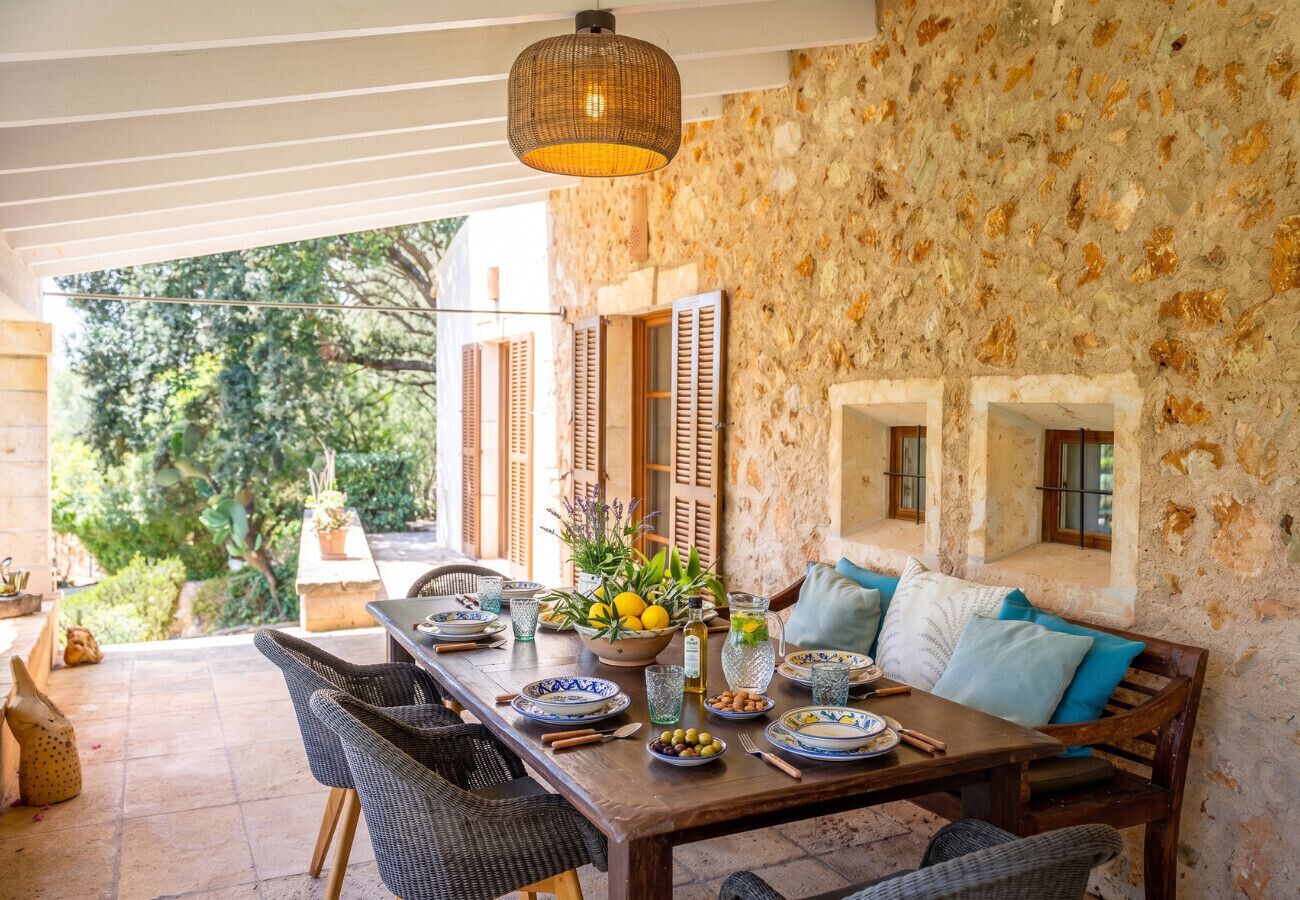 Un espace extérieur aménagé pour les repas, avec un mur en pierre, des meubles en osier et une table dressée avec des assiettes, des verres et un saladier rempli de fruits.