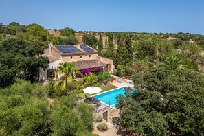 Une maison en pierre avec une piscine, entourée d’une végétation luxuriante et de collines.