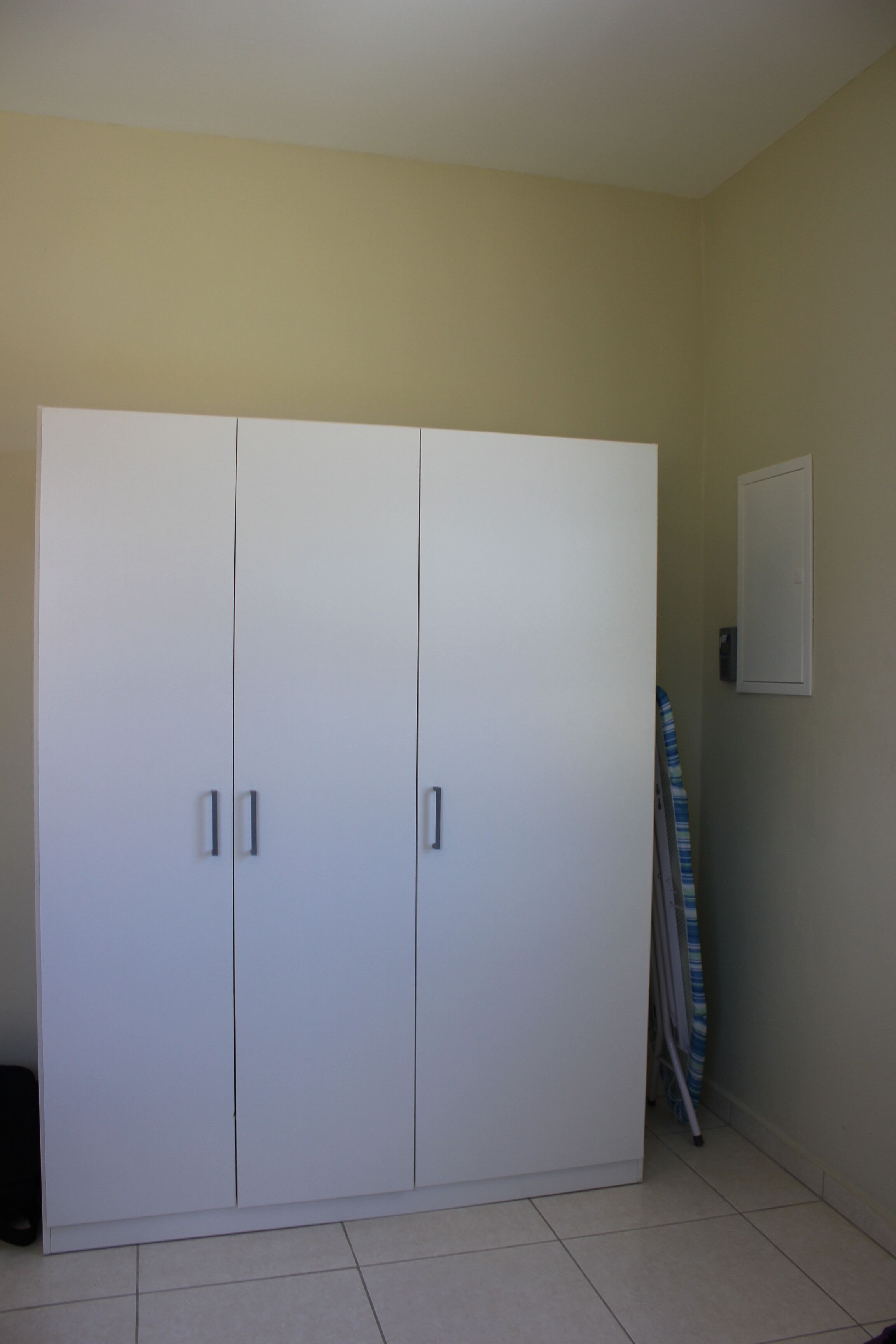 A room with a large white wardrobe, a door, and a wall-mounted electrical outlet.