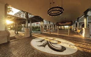 Een ruime lobby met een groot rond embleem op de vloer, een overdekt zitgedeelte en een moderne kroonluchter.