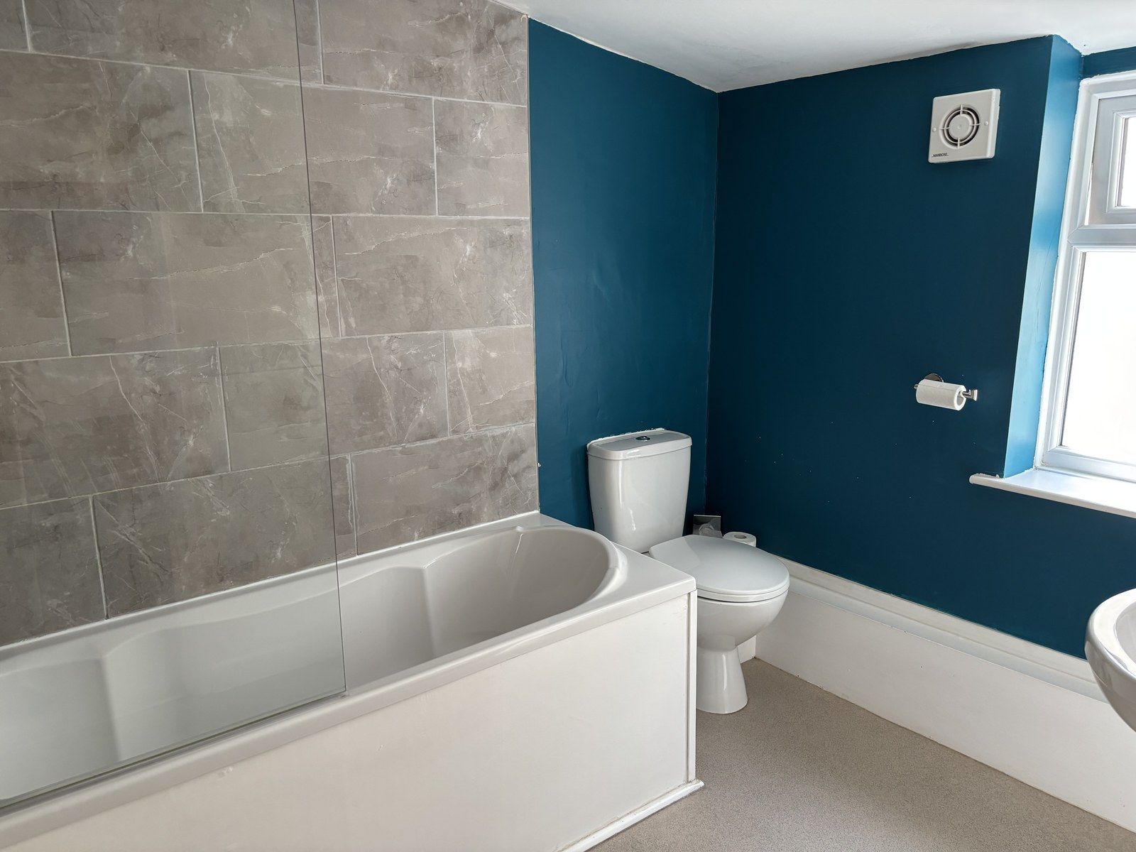 A bathroom with a bathtub, toilet, and a window.