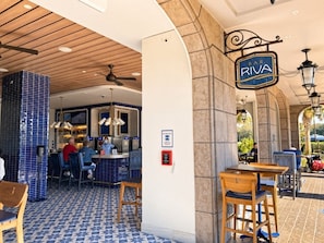 Interno di un ristorante con pareti in piastrelle blu, soffitto in legno e zona bar con un cartello che riporta la scritta 'BAR RIVA'.