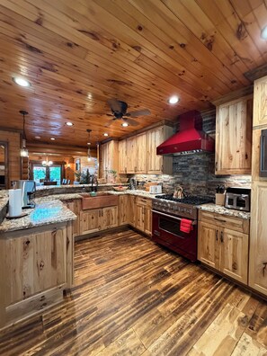 A spacious kitchen with wooden cabinets, granite countertops, a red stove, and a stone backsplash.