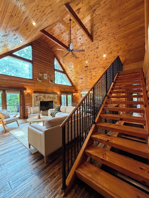 Un amplio salón con una escalera de madera, ventanas grandes y una chimenea.