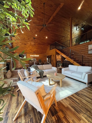 A spacious living area with a high ceiling, wooden flooring, and a staircase leading to an upper level.