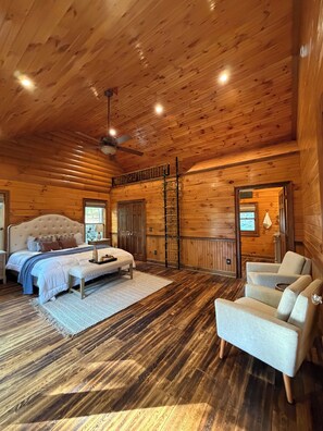 A log cabin bedroom with a bed, a chair, a ladder, and a ceiling fan.