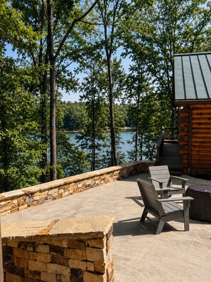 A lakeside patio with stone walls, a wooden deck, and a view of the lake and trees.