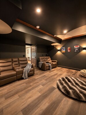 A modern home theater room with dark walls, wooden flooring, and leather recliners.