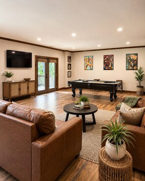 A living room with a pool table, leather sofas, a flat-screen TV, and artwork on the walls.
