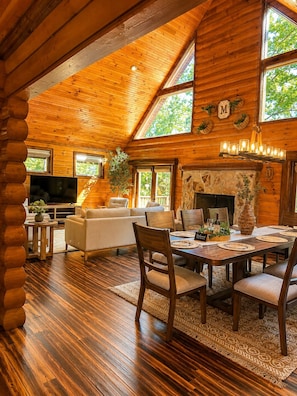 A log cabin interior with a dining area, fireplace, and a television in the living room.