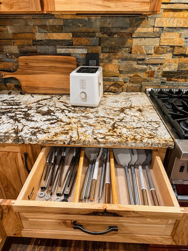 A kitchen with a stone backsplash, a white toaster, and a drawer organizer with utensils.