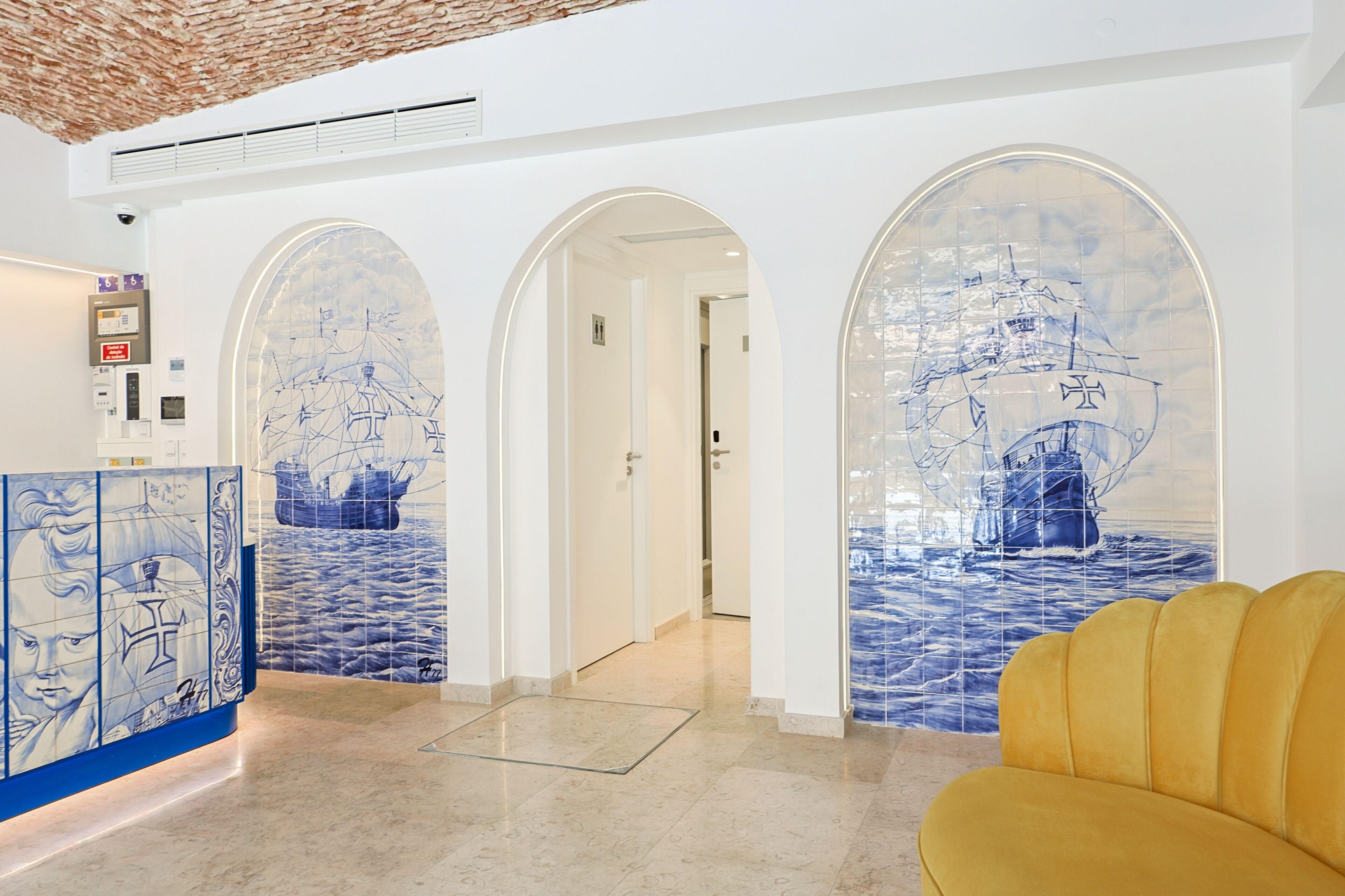 Un hall de hotel con un mural temático náutico, una mesa de recepción y un sillón amarillo.