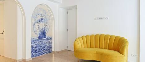 A room with a yellow sofa, a tiled floor, and a wall with a ship mural.