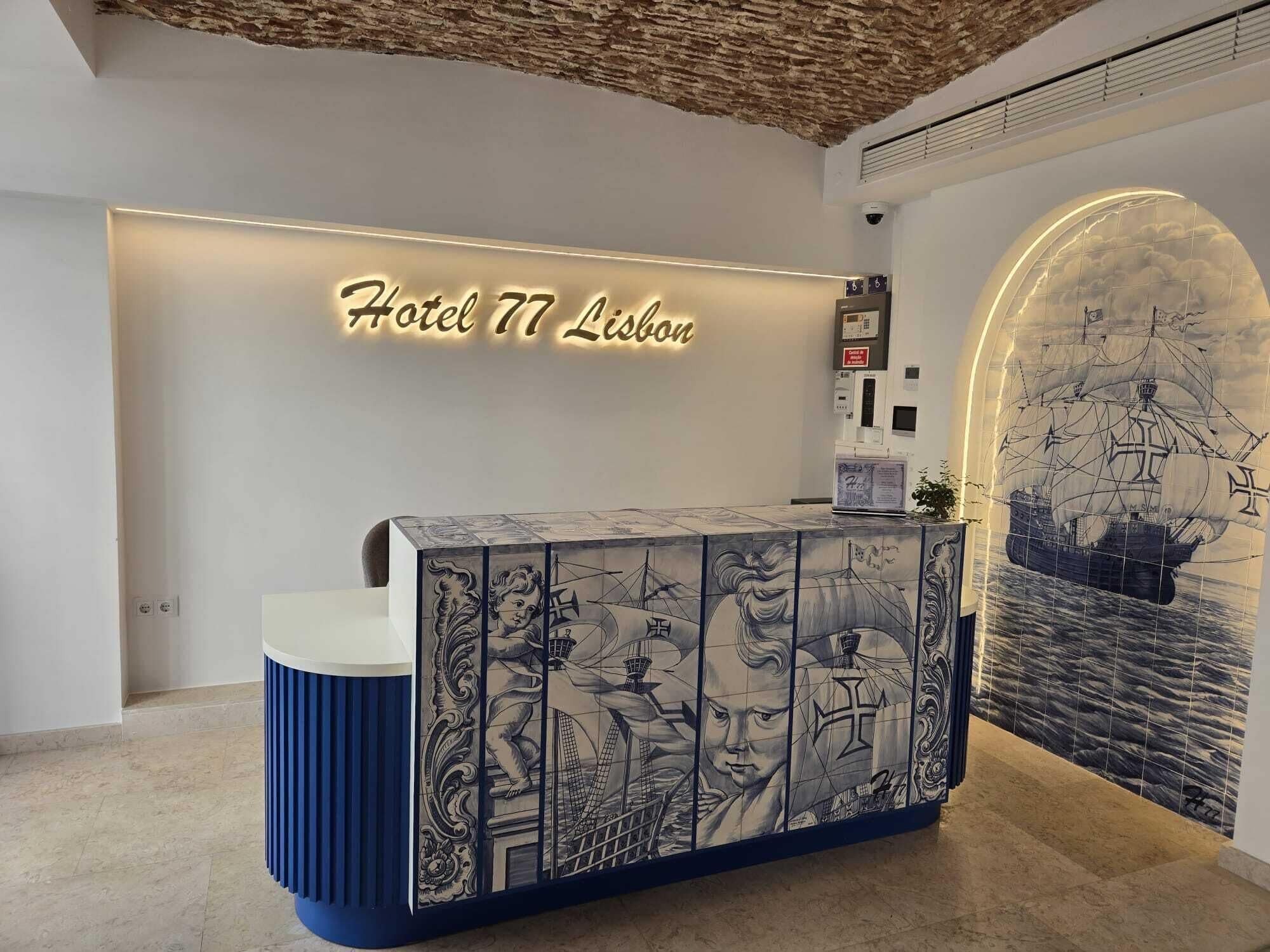 A reception desk with a sign reading 'Hotel 77 Lisbon' and a mural of a ship on the wall.