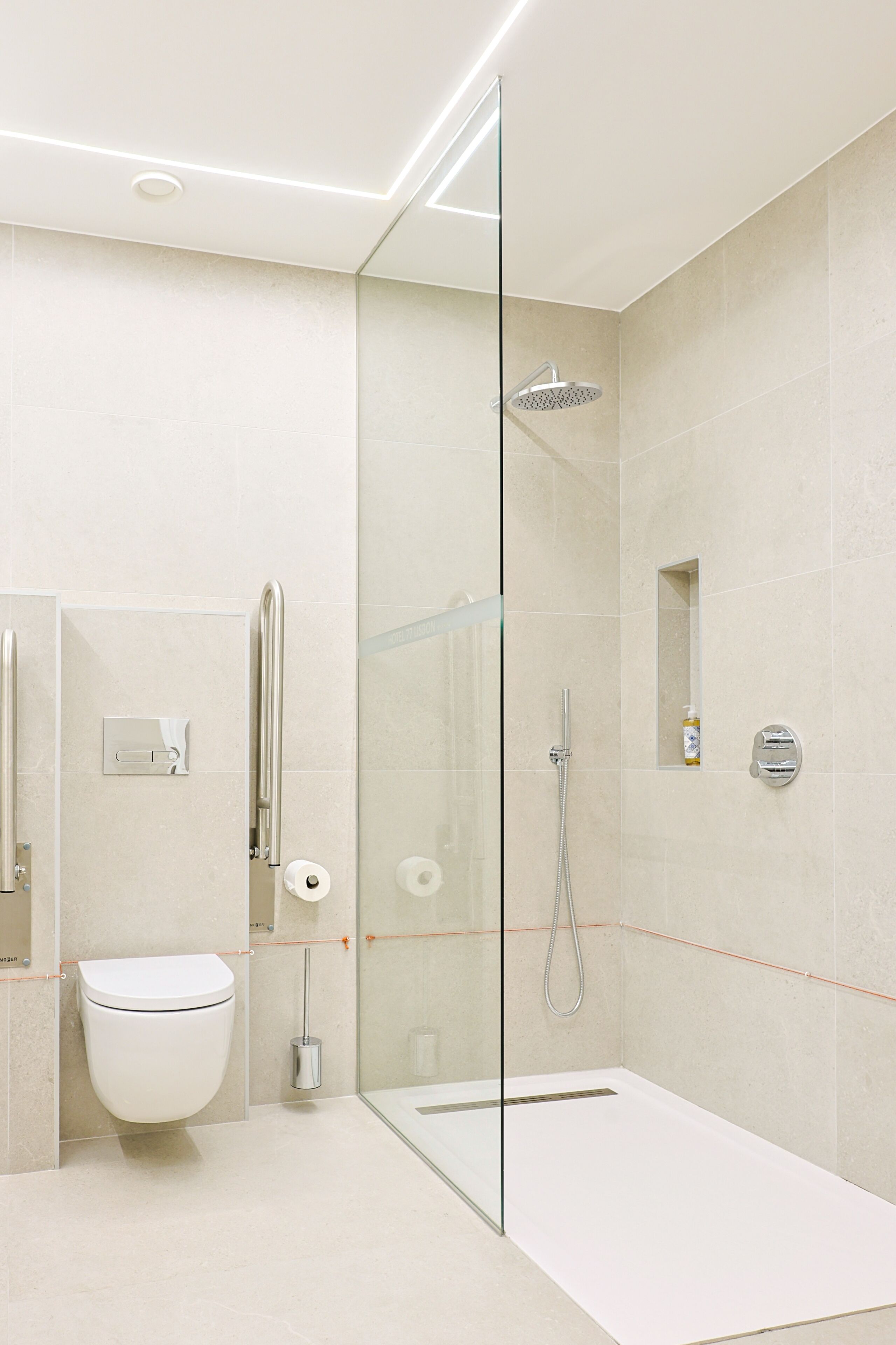 A modern bathroom with a glass-enclosed shower, a toilet, and a hand dryer.