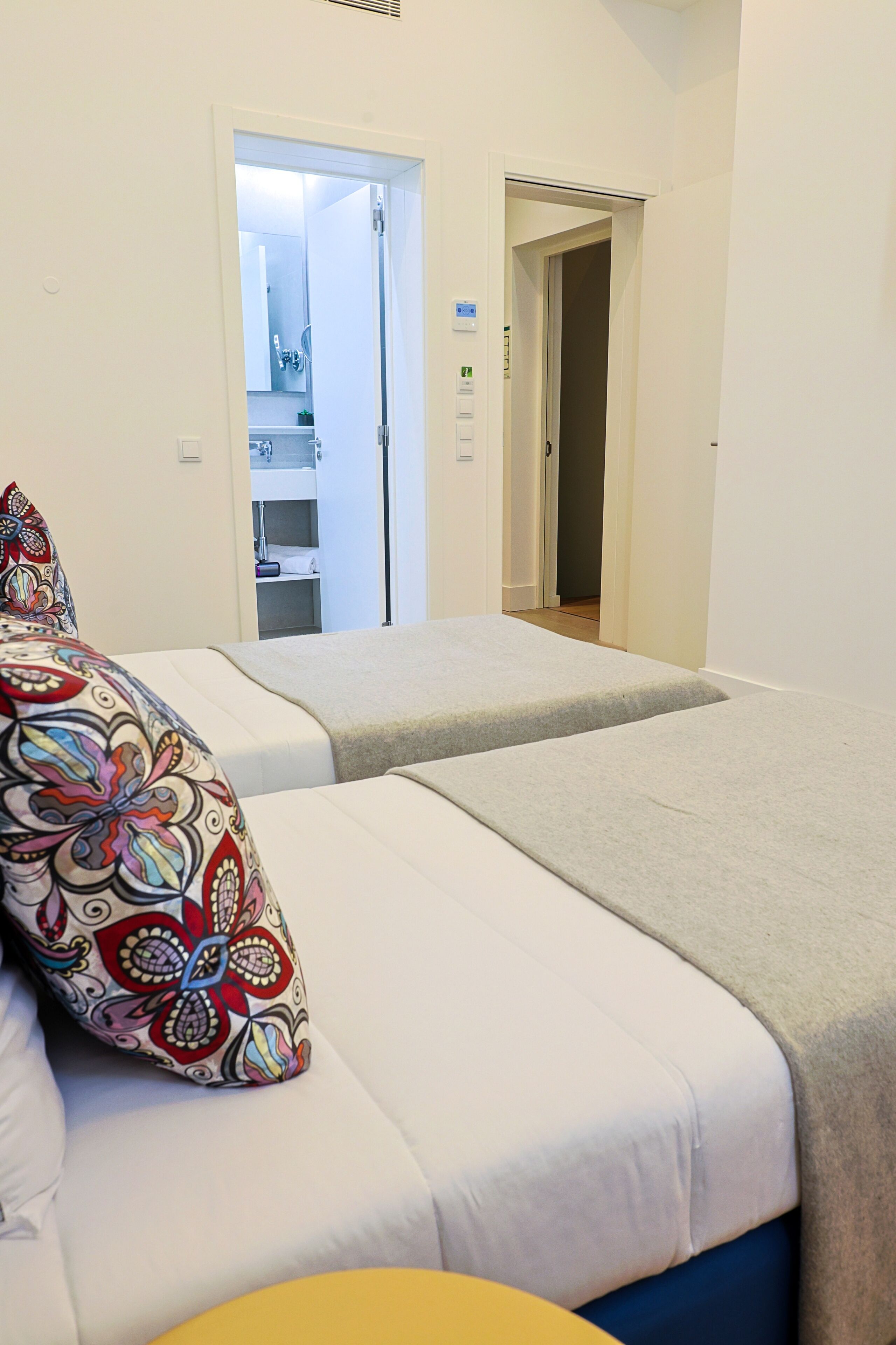 A hotel room with two beds, a bathroom visible through an open door, and a small table with a colorful pillow.