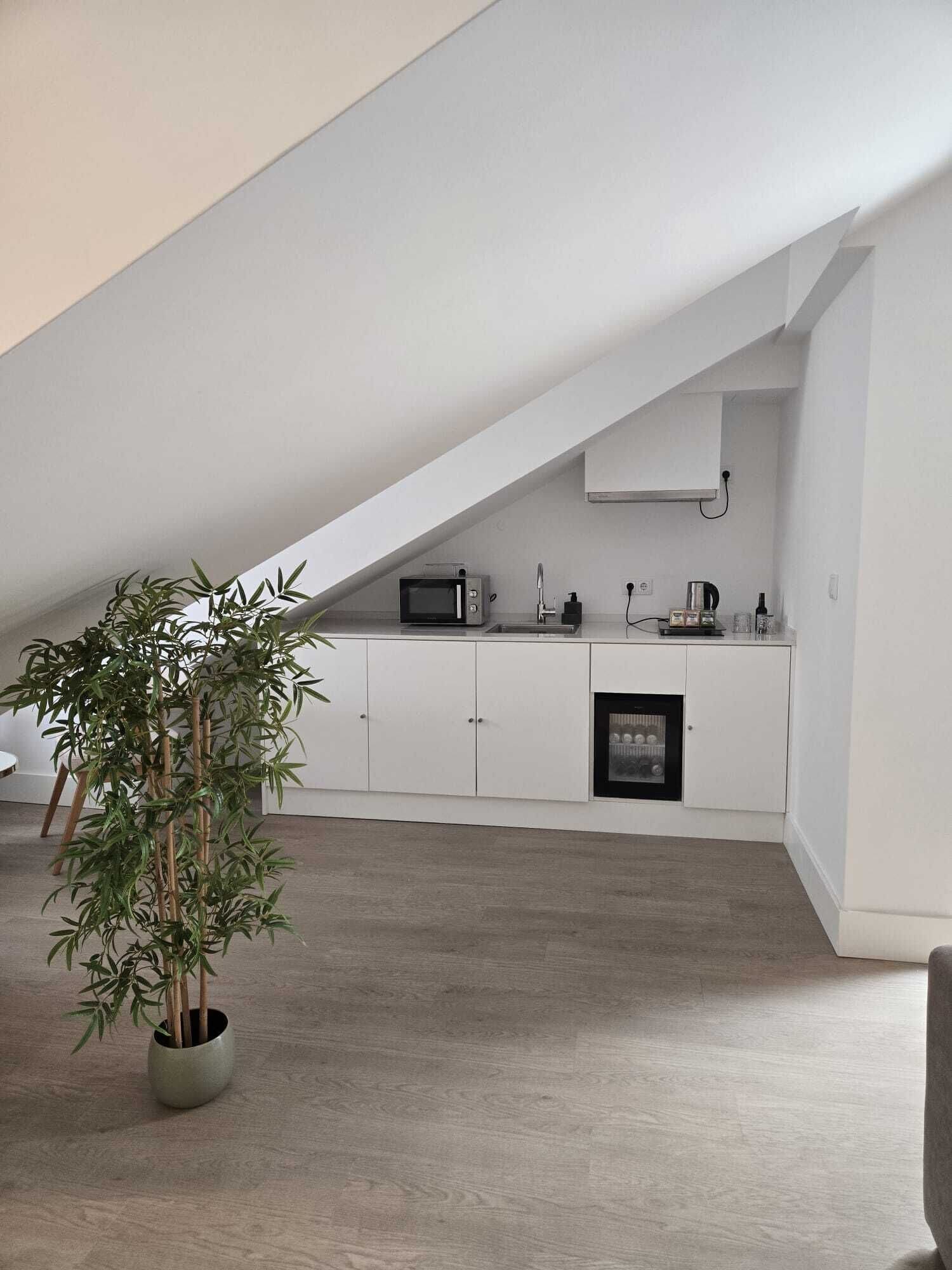 A modern kitchen with white cabinetry, a microwave, a sink, and a small refrigerator. There is a bamboo plant in a pot on the floor.