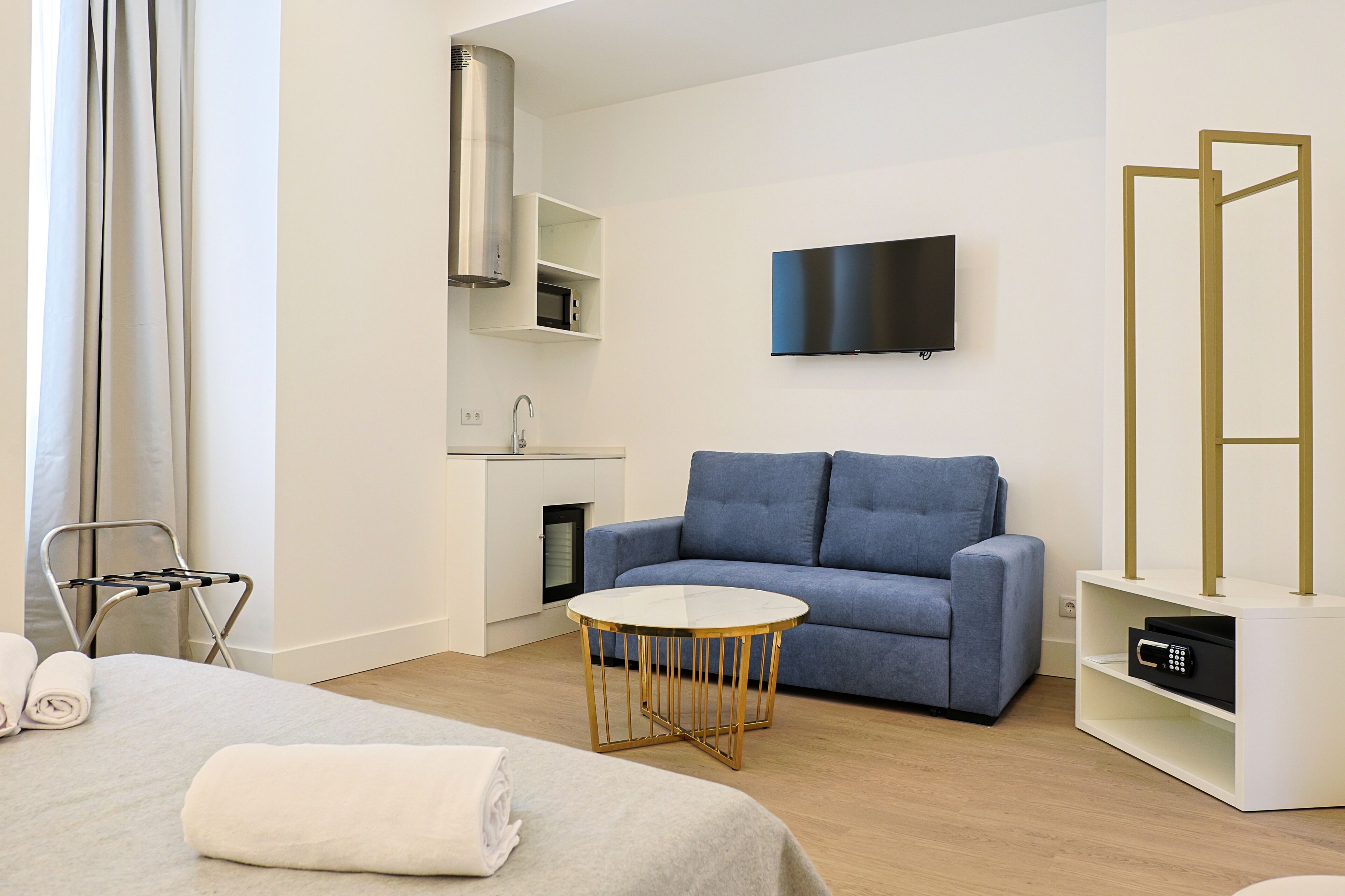 Ein modernes Hotelzimmer mit einer Couch, einem kleinen runden Tisch, einem flachbildfernseher an der Wand, einer eingebauten Mikrowelle und einem Minikühlschrank.